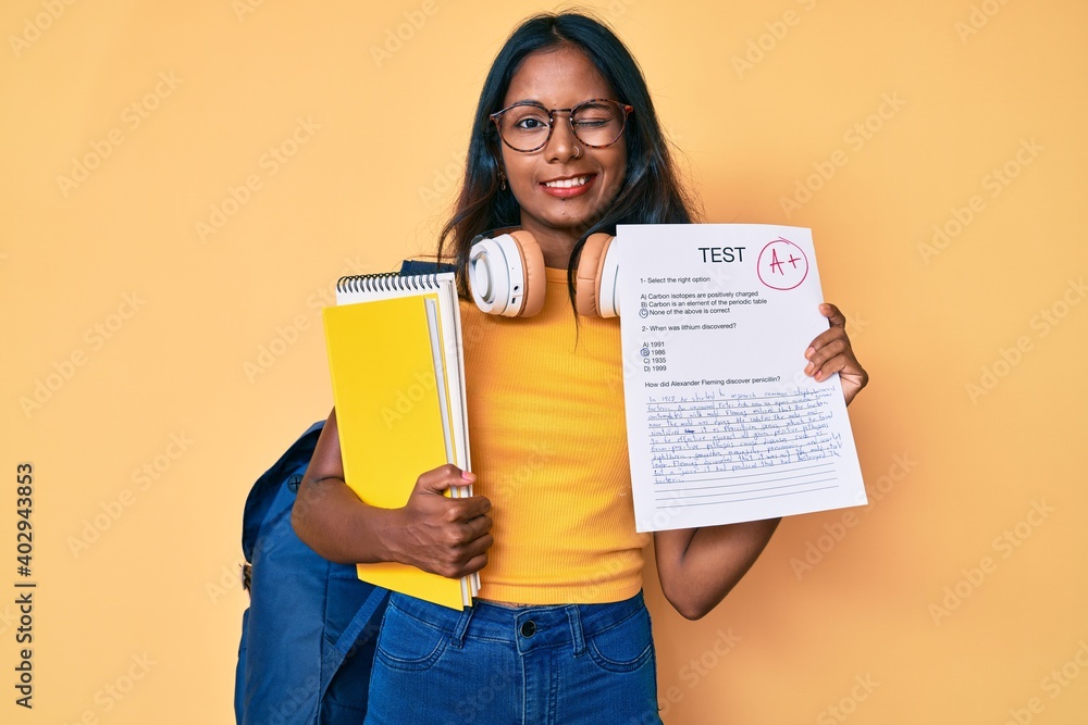 Young indian girl wearing backpack showing a passed exam winking looking at the camera with sexy expression, cheerful and happy face. Young indian girl wearing backpack showing a passed exam winking looking at the camera with sexy expression, cheerful and happy face.