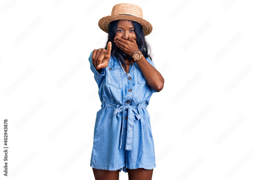 Young indian girl wearing summer hat laughing at you, pointing finger to the camera with hand over mouth, shame expression Young indian girl wearing summer hat laughing at you, pointing finger to the camera with hand over mouth, shame expression