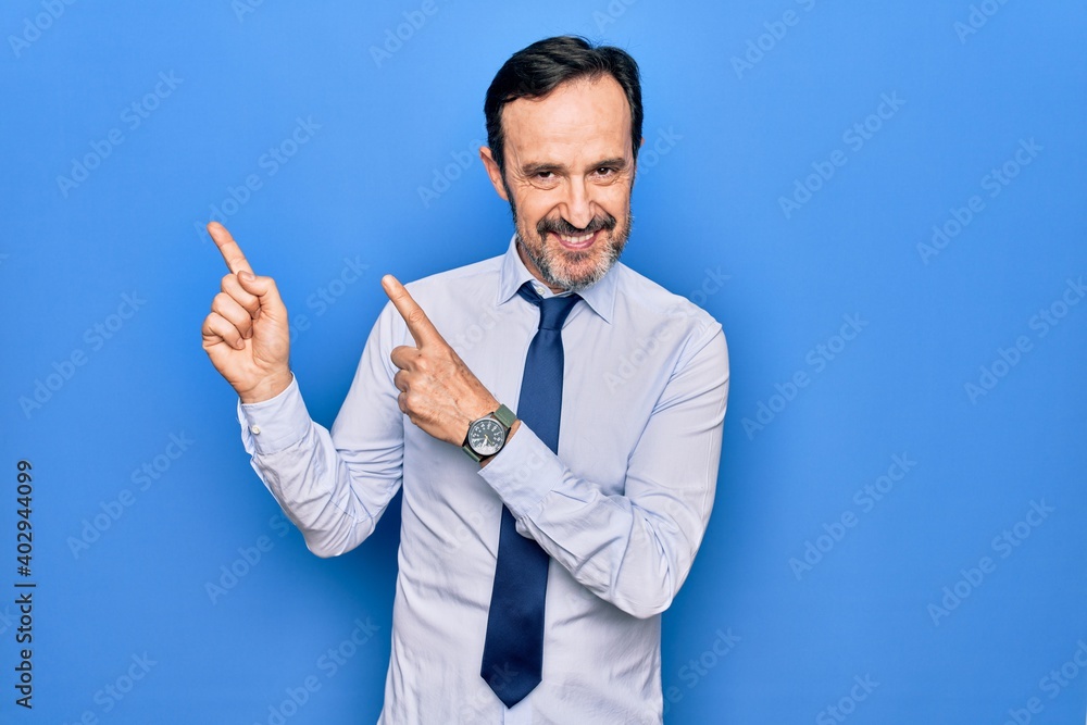 Middle age handsome business man wearing elegant tie standing over isolated blue background smiling and looking at the camera pointing with two hands and fingers to the side. Middle age handsome business man wearing elegant tie standing over isolated blue background smiling and looking at the camera pointing with two hands and fingers to the side.