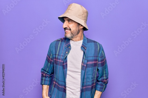 Middle age handsome man wearing casual shirt and hat over isolated purple background looking to side, relax profile pose with natural face and confident smile.