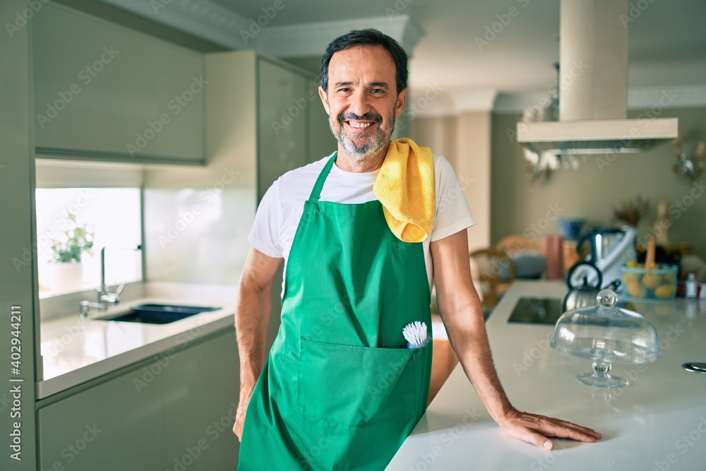 Middle age housekeeping man with beard smiling happy standing at the kitchen Middle age housekeeping man with beard smiling happy standing at the kitchen