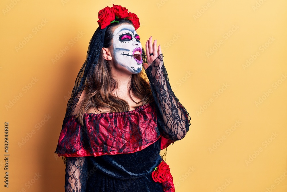 Young woman wearing day of the dead costume over yellow shouting and screaming loud to side with hand on mouth. communication concept.