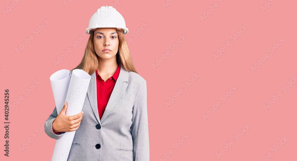 Beautiful young woman wearing architect hardhat holding build project thinking attitude and sober expression looking self confident