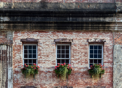 Beautiful flower boxes adorn three windows of an old, rustic brick building in a southern US city.
