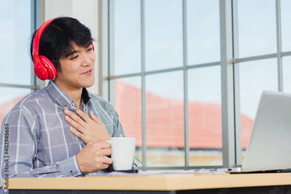 Asian young businessman happiness with red headphones sitting on desk workplace home office with a laptop computer, confident handsome man lifestyle smile relax holding a coffee cup, listens to music Asian young businessman happiness with red headphones sitting on desk workplace home office with a laptop computer, confident handsome man lifestyle smile relax holding a coffee cup, listens to music