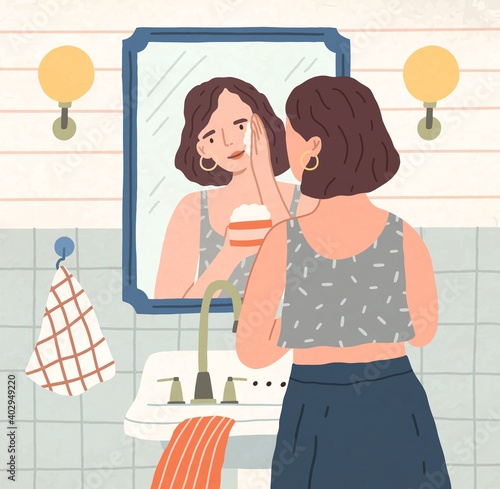 Yong beautiful woman moisturizing or washing her face with cream or cleansing lotion in front of mirror. Daily beaty routine and skin care at home. Colored flat vector illustration