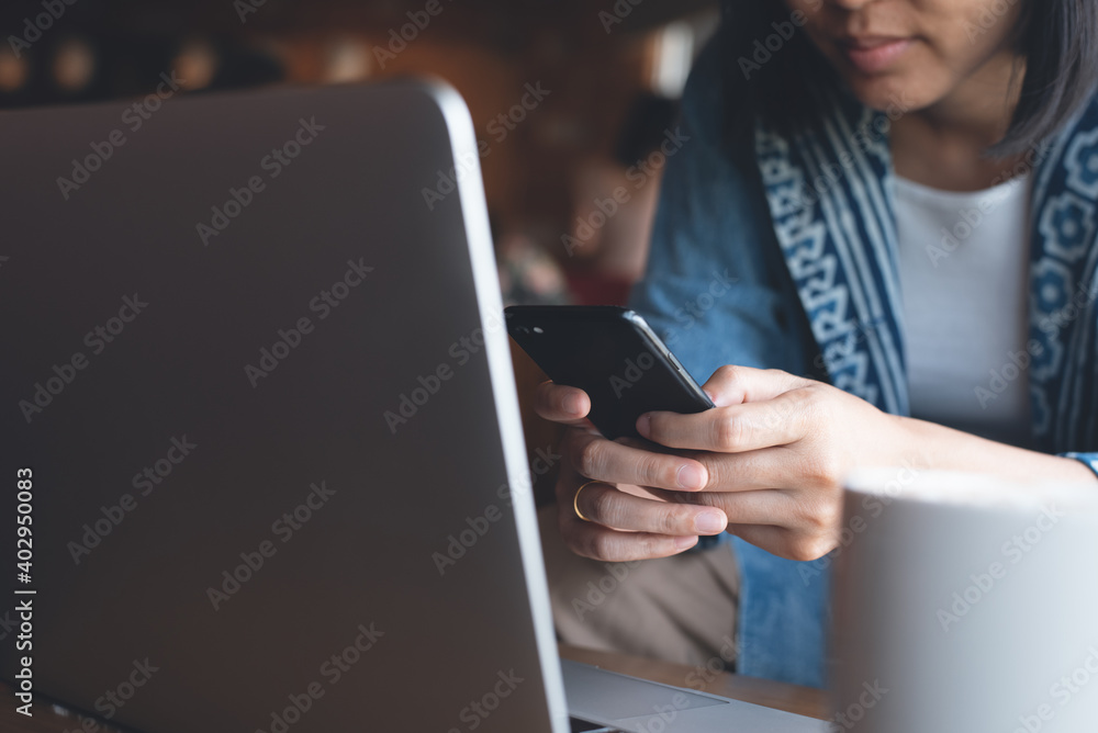 Young asian woman using mobile phone and working on laptop computer at coffee shop