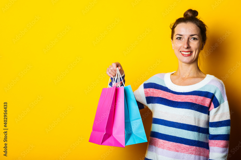 Young woman in sweater holding shopping bags on yellow background Young woman in sweater holding shopping bags on yellow background