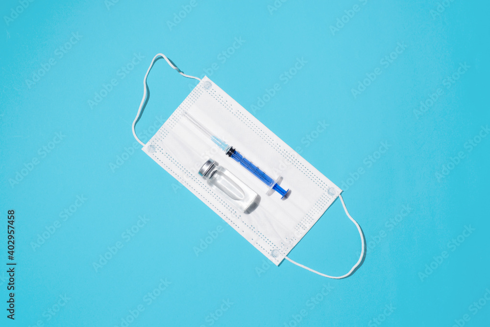 Population vaccination, healthcare and medicine concept. Vaccine vial, syringe and medical face mask on blue background, flat lay Population vaccination, healthcare and medicine concept. Vaccine vial, syringe and medical face mask on blue background, flat lay