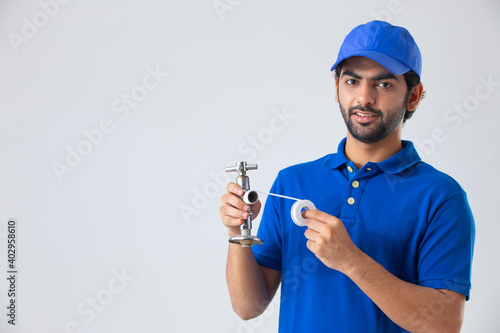 A PLUMBER LOOKING AT CAMERA WHILE FIXING A TAP	 photo