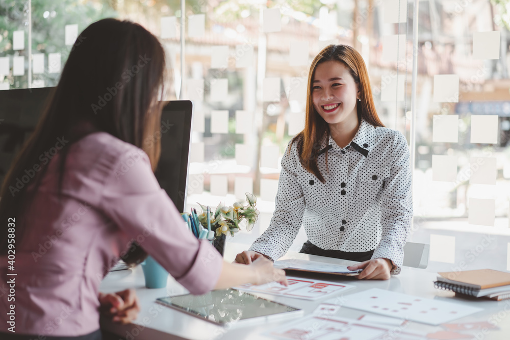 Two young asian women colleagues in smart casual wear planning business strategy together at the modern coworking space.