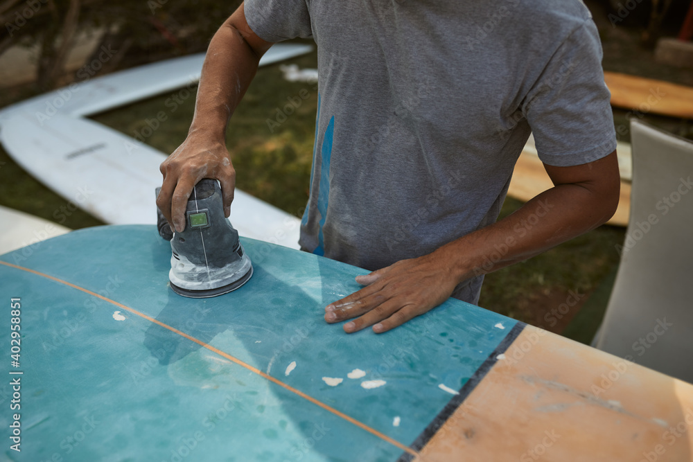 Hawaiian tanned man repairs surfboard, hands close up