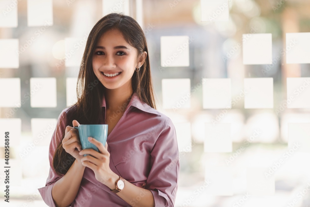 Portrait of confident smiling asian business woman in casual wear holding a cup of coffee at modern office.