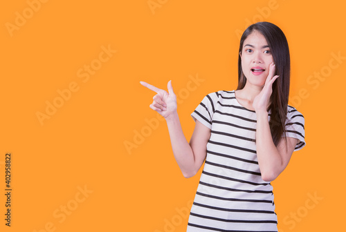 Smiling asian woman pointing up and looking at the camera over yellow background