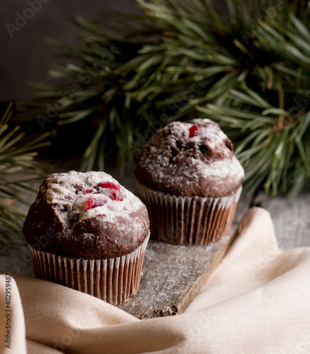 Muffins with red berries next to fir branches on a wooden background.
