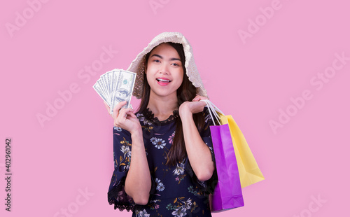 Asian young woman with a lot of money in her hand holding a shopping bag smiling happily on the pink background.