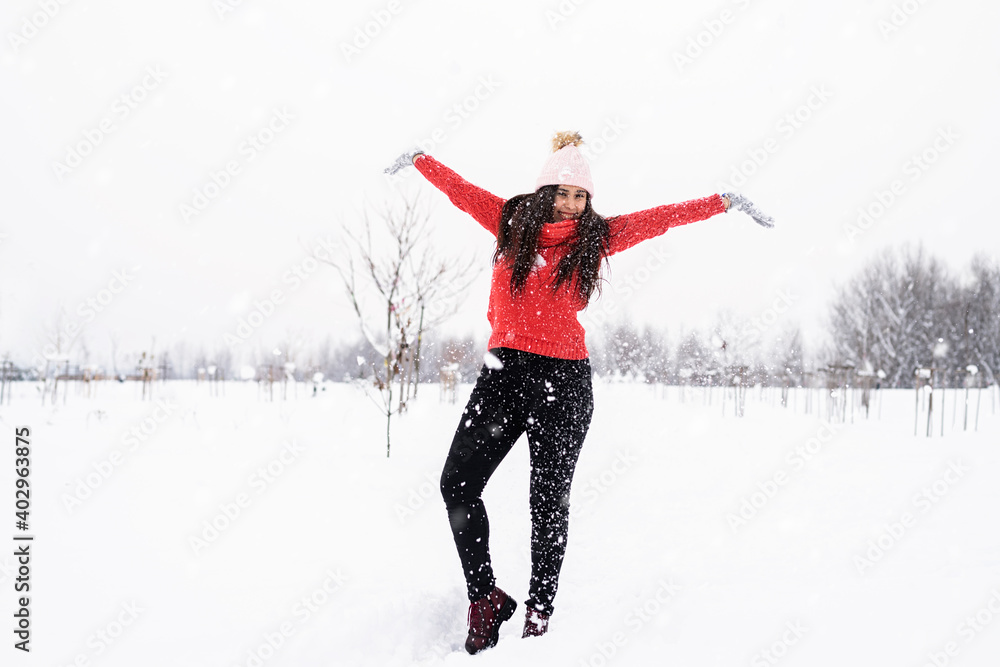 Young brunette woman in red sweater playing with snow in park