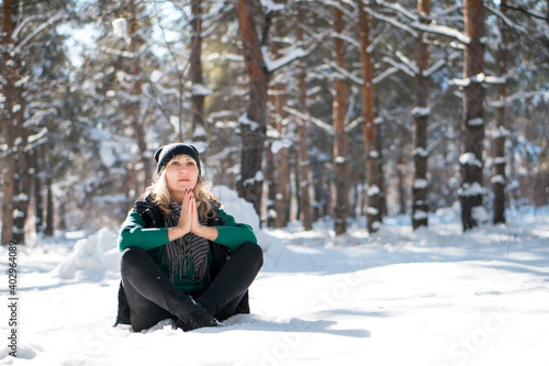 Young woman meditates in snowy forest or park.