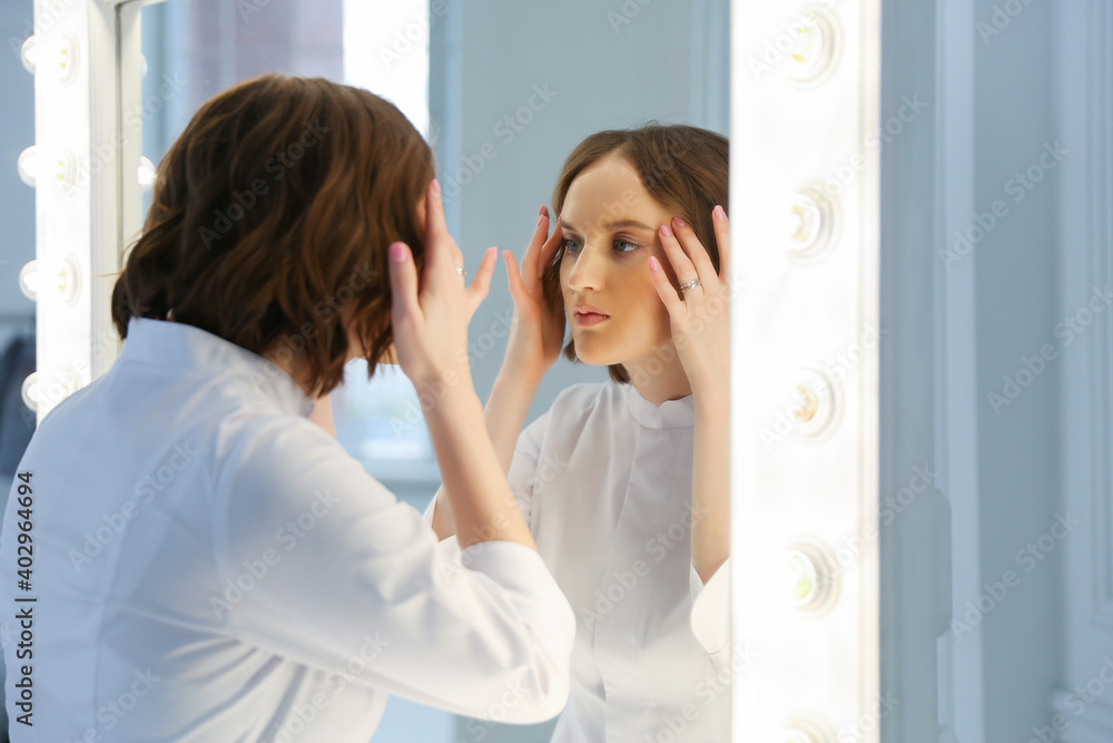 woman examines the skin of her face in the mirror. doctor beautician with well-groomed face skin looks in the mirror. the girl enjoys the beauty of her skin.