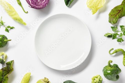 Frame fresh vegetables around white plate on white background. Top view photo