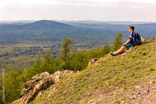 a young male tourist sits on the top of the sugomak mountain and looks into the distance at the Ural mountains on a summer day photo