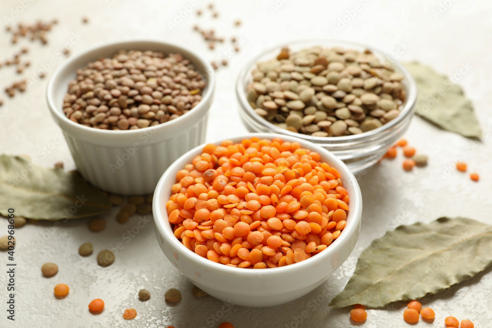 Bowls with different legumes and bay leaves on white textured background Bowls with different legumes and bay leaves on white textured background