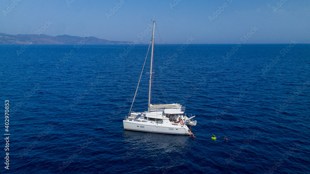 Catamaran sailing in blue, turquoise water in Greece, beautiful catamaran during summer holiday, view from drone