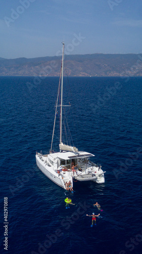 Catamaran sailing in blue, turquoise water in Greece, beautiful catamaran during summer holiday, view from drone