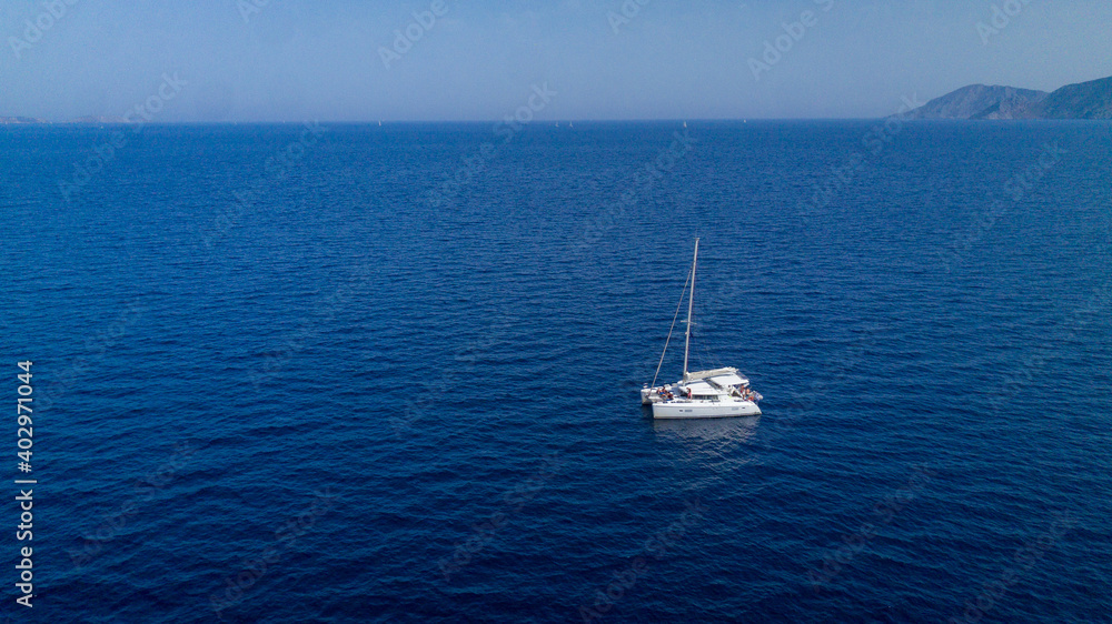 Catamaran sailing in blue, turquoise water in Greece, beautiful catamaran during summer holiday, view from drone Catamaran sailing in blue, turquoise water in Greece, beautiful catamaran during summer holiday, view from drone