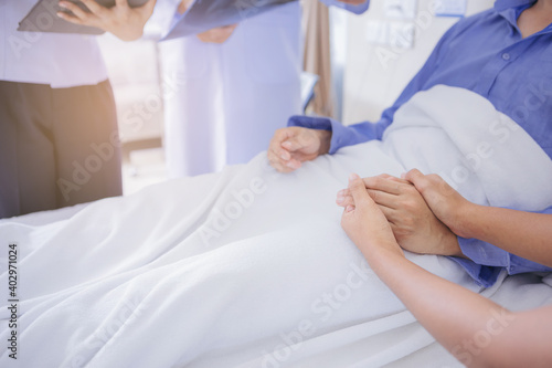 Doctor and nurse talk with husband patient about examining result from doctor, family health care, palliative care, with wife holding hand of patient at hospital