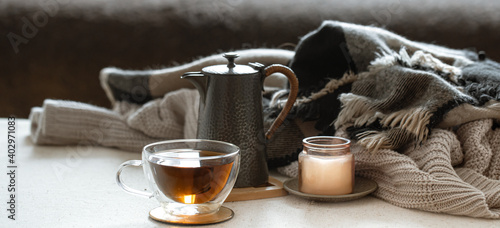 Cozy home composition with a cup of tea, teapot, candlestick and knitted elements.
