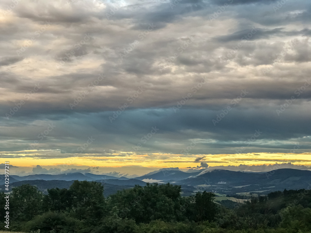 The landscape of the Beskydy Mountains from the viewpoint near Jicin during a rainy afternoon full of dark clouds in the sky and a view of the surrounding landscape.