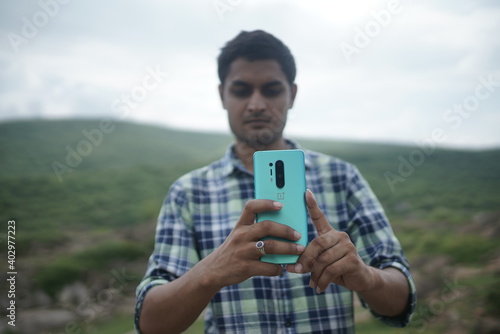 dausa, Rajasthan, India - august 15 , 2020 Happy male using smartphone at mountains, he chatting Online Messaging on mobile. photo