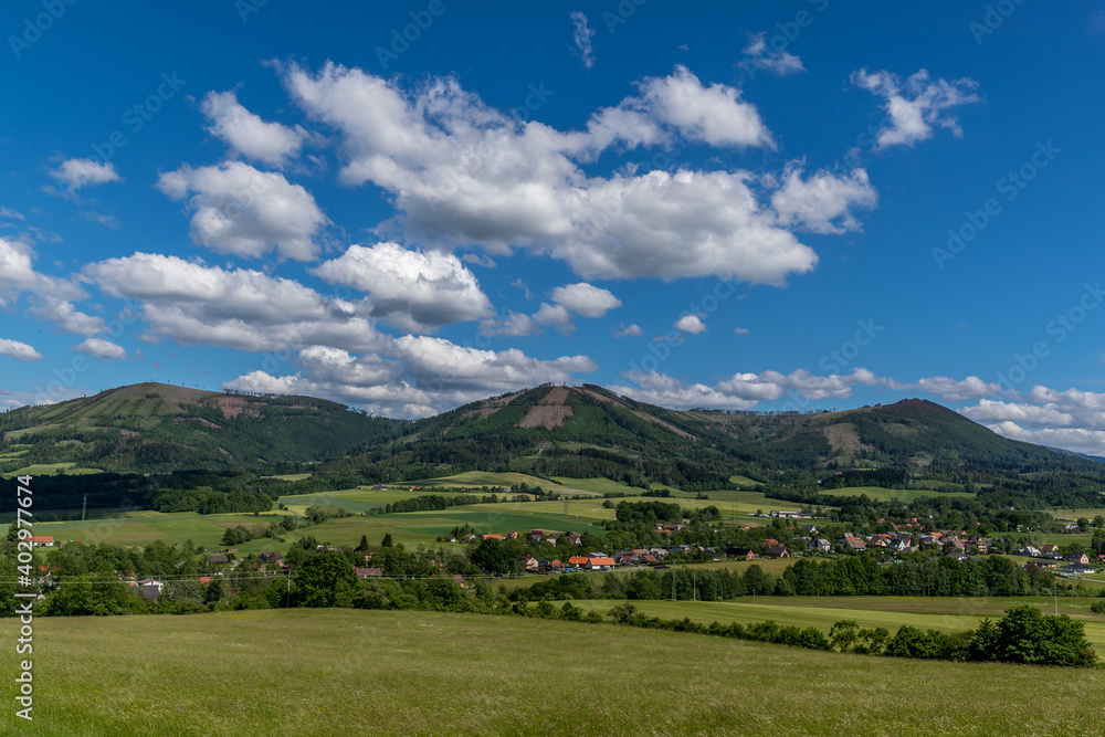 Ondrejnik and views of other Beskydy hills and mountains with white clouds and blue sky in the background during a sunny day.