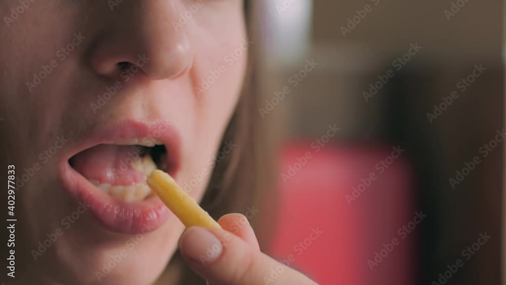 Young woman eating French fries. Close-up shows her mouth where she puts and eats potatoes with pleasure. Young woman eating French fries. Close-up shows her mouth where she puts and eats potatoes with pleasure.