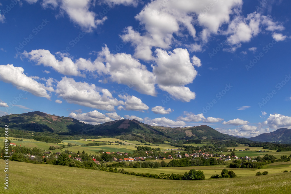 Ondrejnik and views of other Beskydy hills and mountains with white clouds and blue sky in the background during a sunny day.