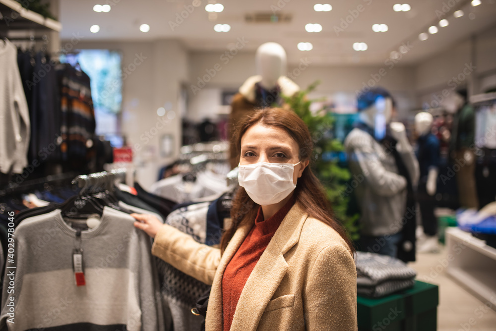 Beautiful girl wearing protective medical mask and fashionable clothes looks at behind of showcase. New normal lifestyle concept.