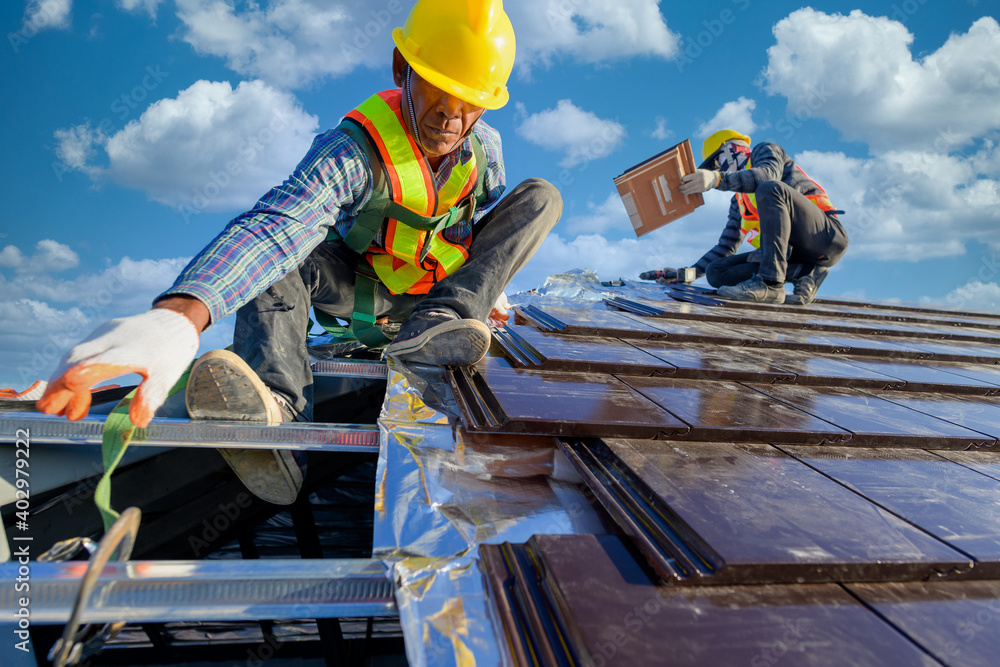 Fototapeta premium Two male workers wearing safety clothes Installing the roof tile house That is a ceramic tile roof On the construction site