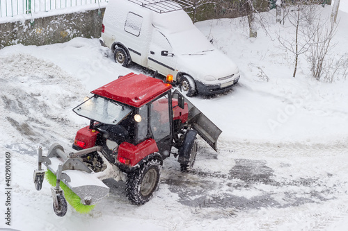 Small red tractor with snow plow in courtyard during snowfall