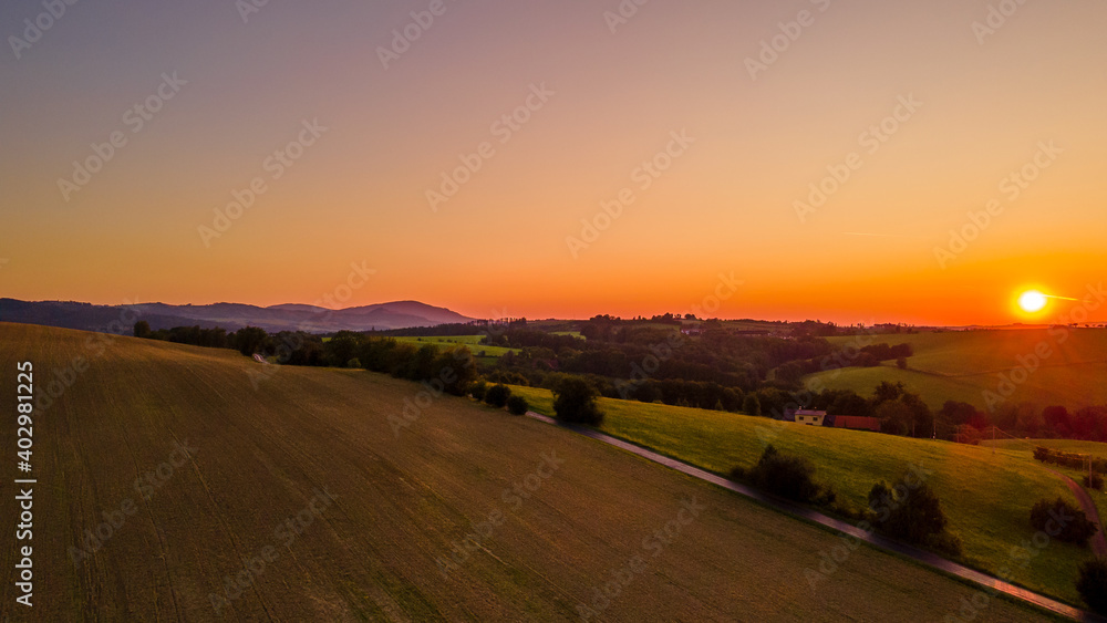 Aerial landscape view at orange sunset with field and village lying in the background. Aerial landscape view at orange sunset with field and village lying in the background.