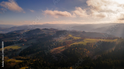 Aerial view of hilltops during sunrise rays shine through the landscape through clouds on the ground during the autumn morning Beskydy region.