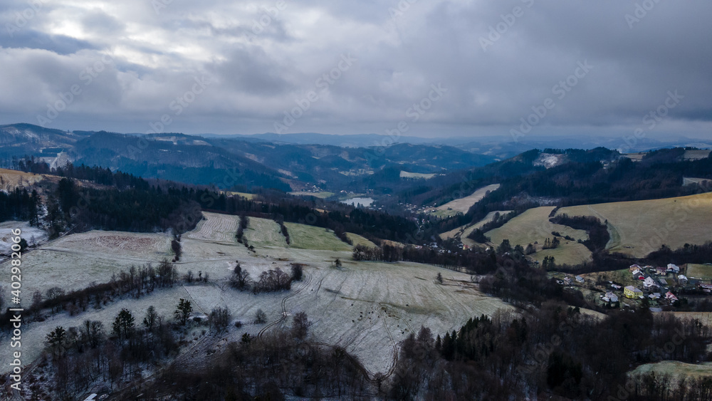 Aerial view of a hilly landscape with freshly fallen snow during a light snowfall in the Beskydy region.