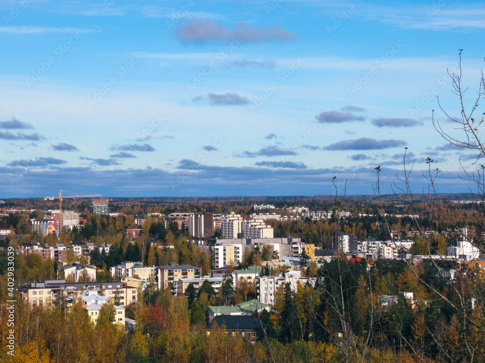 City panorama with apartment buildings, trees in autumn colors and blue sky with some clouds.