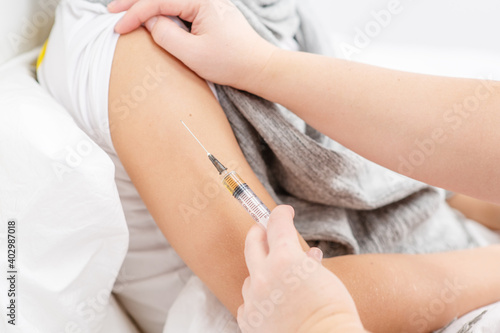 Close up image a sick boy is given a shot in the forearm during treatment. An unhealthy child at home. Cold season.
