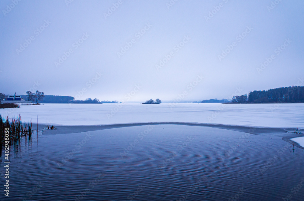 Winter landscape of frozen lake with island in the evening