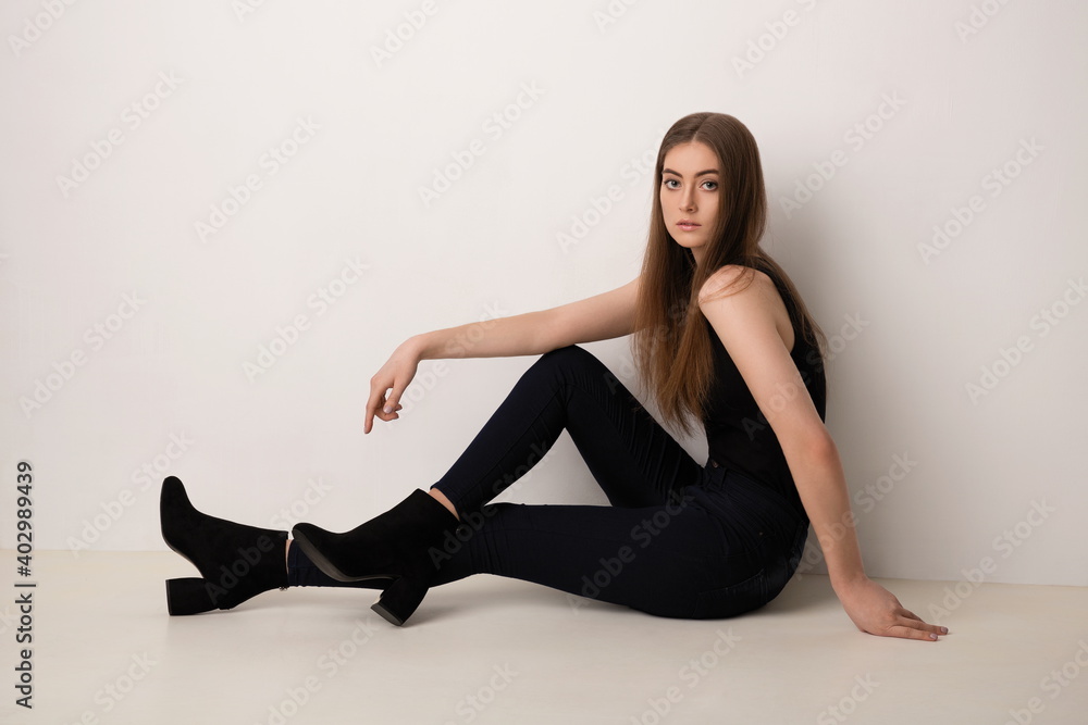 beautiful girl with exquisite makeup in black clothes posing sitting against a white wall beautiful girl with exquisite makeup in black clothes posing sitting against a white wall