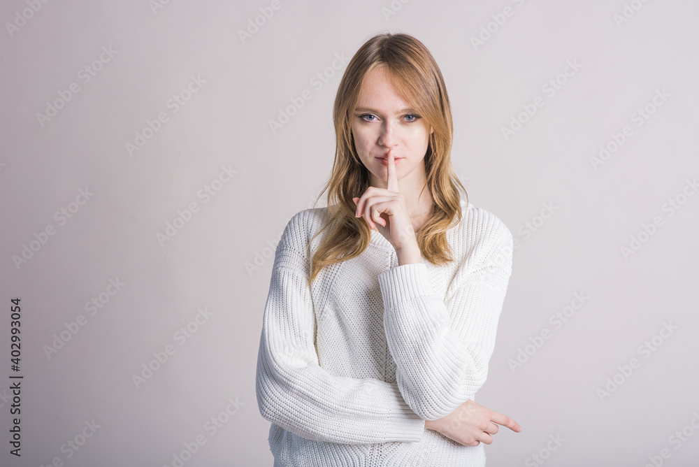 Portrait of a stylish girl on a white background in the studio who makes a gesture with the index finger above the mouth Portrait of a stylish girl on a white background in the studio who makes a gesture with the index finger above the mouth