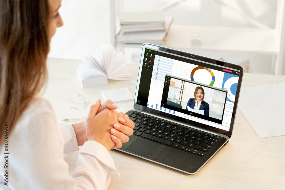 Fototapeta premium Video conference. Virtual meeting. Corporate webinar. Lockdown WFH. Female partners working from home with charts graphs on laptop at light modern workplace.
