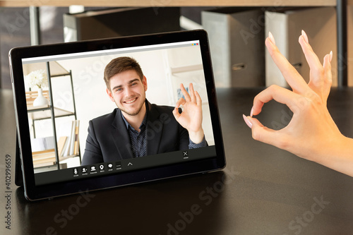 Web chat. Successful partnership. Online cooperation. Virtual meeting. Colleagues approving agreement with OK gesture on tablet screen at modern home office workplace. photo