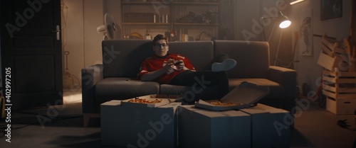 POV Portrait of Caucasian teenager playing video game inside home garage, enjoying pizza. Shot with 2x anamorphic lens photo